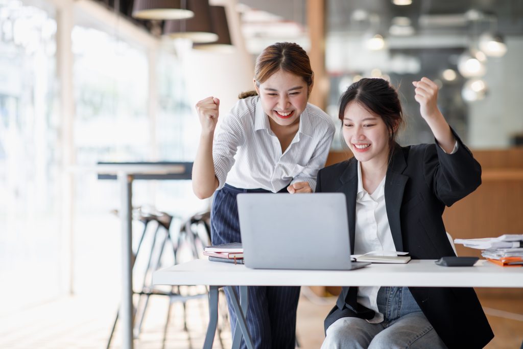 Euphoric winner watching a laptop on a desk winning at working in an office, Asian Teamwork, coworke